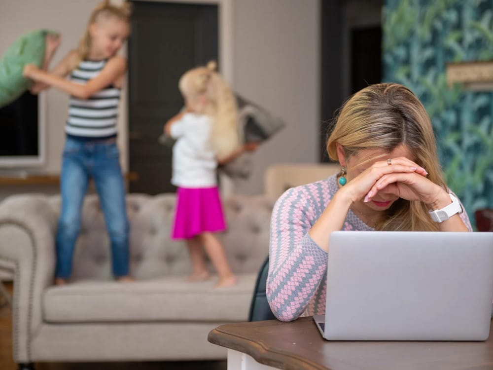 Mãe tentando trabalhar em casa no computador e os filhos ao fundo fazendo barulho.