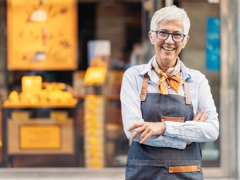 Empreender após os 40 anos. Mitos do Empreendedorismo Tardio. Imagem ilustrativa de mulher empreendedora com mais de 40 anos sorrindo em frente a sua loja.