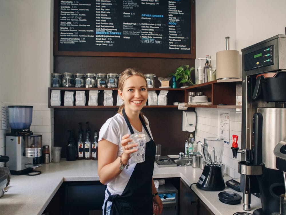 Foto de uma universitária trabalhando como barista em um café