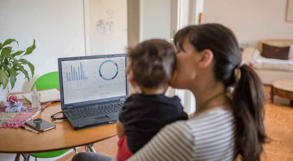 mulher trabalhando no laptop com seu bebê no colo